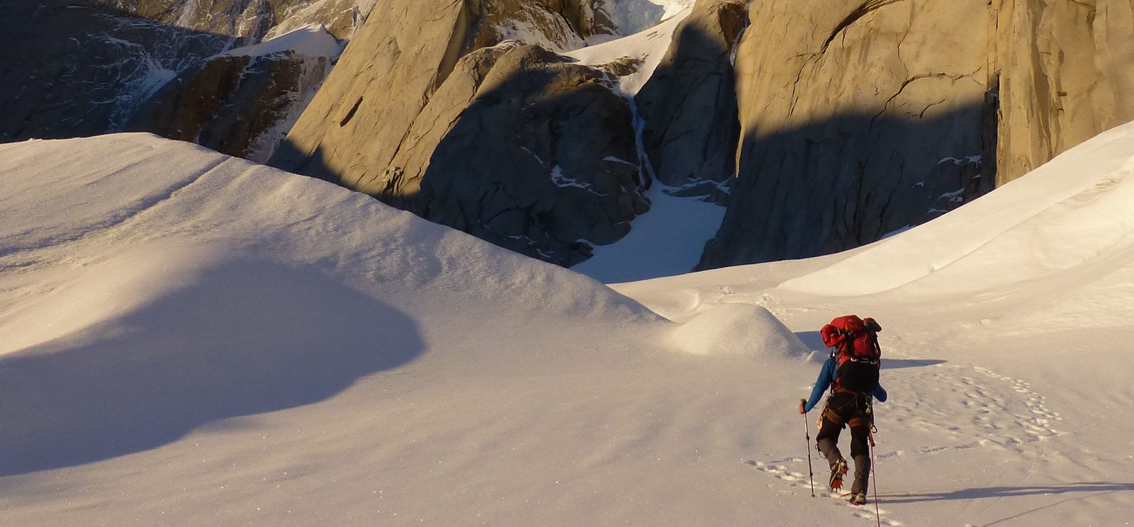 A mountaineer approaching granite cliffs across snow